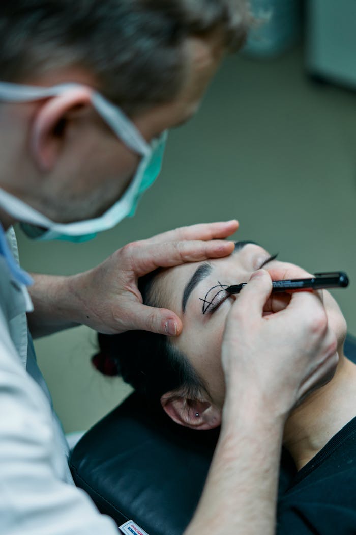 Surgeon marking patient's eyelid for blepharoplasty in medical office.